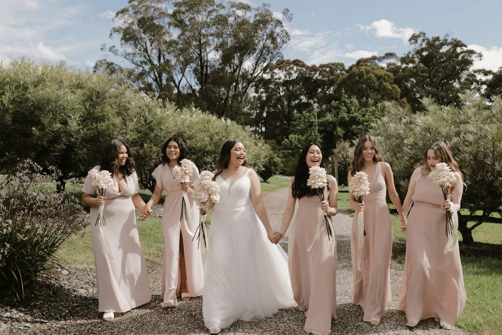 New Zealand bride in white walking with five bridesmaids during wedding celebration
